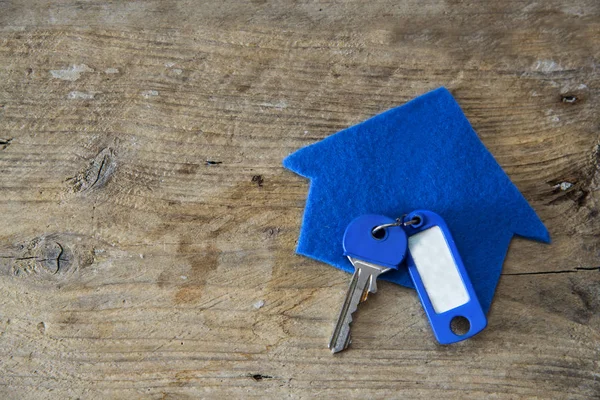 Casa de tecido azul e uma chave com chaveiro em branco em wo rústico — Fotografia de Stock