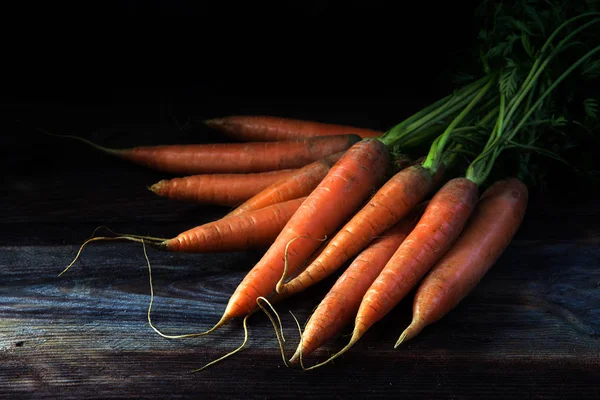 Zanahorias naranjas frescas con hojas verdes sobre madera rústica oscura, fondo negro — Foto de Stock