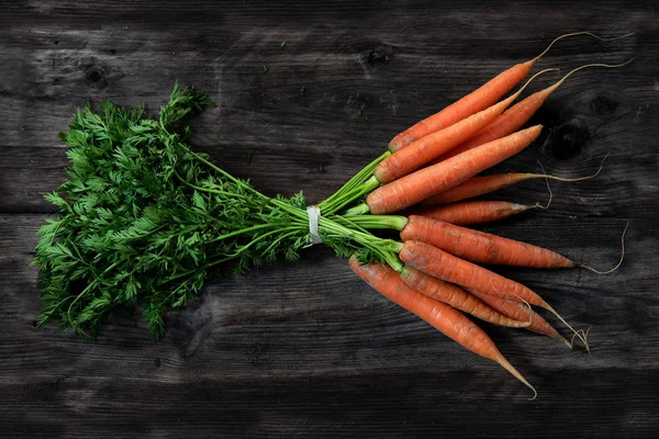 Bos van wortelen met verse groene bladeren op een donkere, grijze houten tafel — Stockfoto