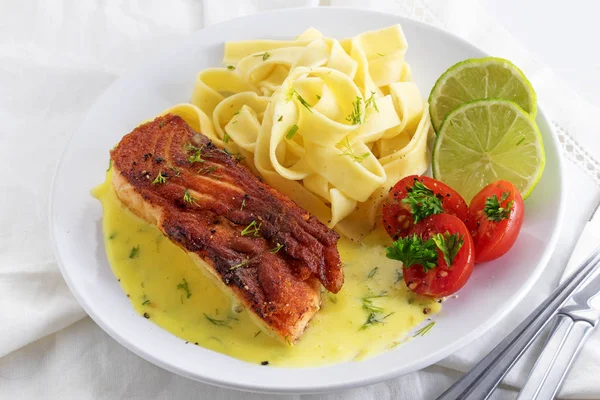 Grillad lax skålen med citronsås och tagliatelle pasta, lime, tomater och dill garnering på en vit duk — Stockfoto