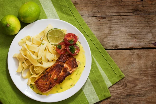 Grilled salmon with herb sauce and tagliatelle pasta, tomatoes and lime on a rustic wooden table, top view from above