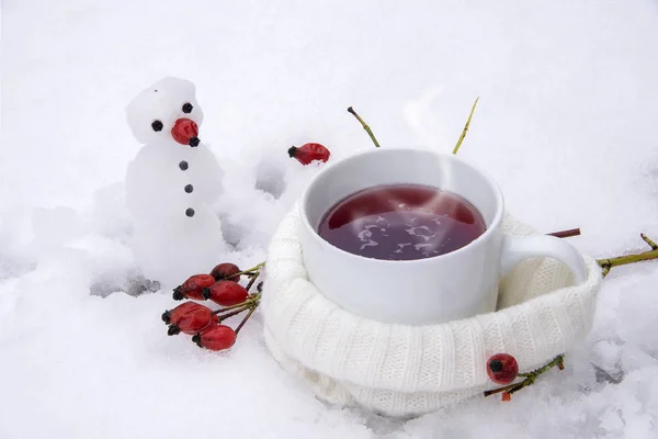 Té caliente con rosa mosqueta roja en la nieve y un poco de muñeco de nieve, bebida de invierno contra la gripe — Foto de Stock