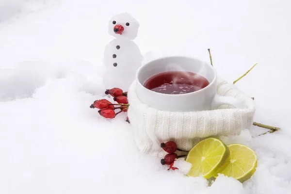 Hot tea with rose hips and lemons outside in the snow and a little snowman — Stock Photo, Image