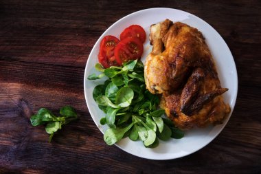 karanlık bir rustik ahşap tahta, yukarıdan havai görünümü üzerinde Mısır salata ve domates ile yarım tavuk ızgara