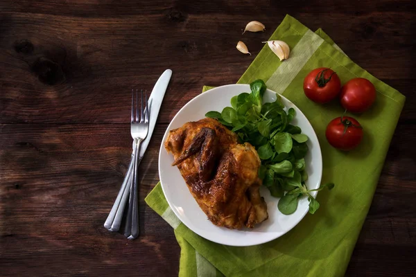 Жареная половина курицы с помидорами, зеленая салфетка, кукурузный салат и чеснок на темном деревенском дереве, вид сверху — стоковое фото