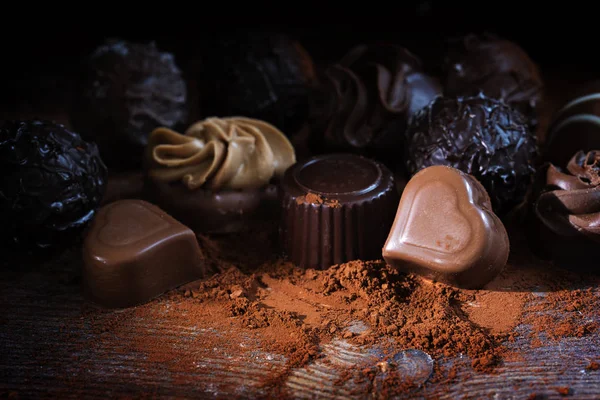 Pralinés de chocolate y cacao en polvo sobre madera rústica como un gif amor, de cerca sobre un fondo oscuro — Foto de Stock