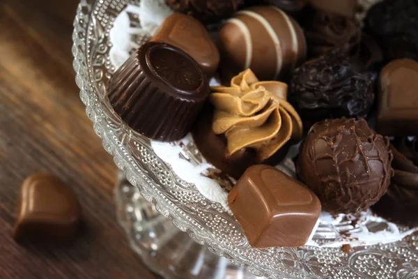 Feine Pralinen aus Schokolade und Nougat, rund und herzförmig als festliches Geschenk auf Glas-Etagere auf rustikalem braunem Holz, Nahaufnahme — Stockfoto