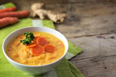 Zencefil kökü, maydanoz garnitür ve kopya alanı bir rustik ahşap masada yeşil peçete ile havuç çorbası