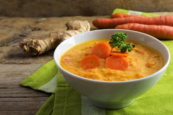 Soupe de carottes à la racine de gingembre, garniture de persil et serviette verte sur bois rustique — Photo