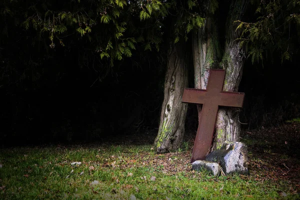 Roestige kruis gemaakt van metaal, leunend tegen oude boomstammen in de schaduw — Stockfoto