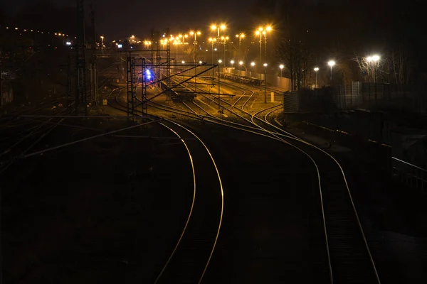 Trilhos ferroviários à noite levam brilhante e curva para uma estação de freigh de carga — Fotografia de Stock