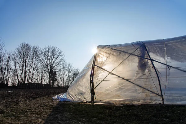 Túnel de estufa de plástico de polietileno retroiluminado pelo sol em um campo agrícola — Fotografia de Stock