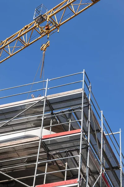 Chantier, bâtiment à plusieurs étages avec échafaudage et grue contre le ciel bleu — Photo