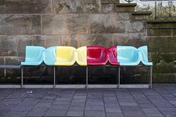 PADERBORN, ALEMANIA, 13 DE MARZO DE 2017: banco con sillas de diseño coloridas frente a una pared de piedra vieja de arena oscura —  Fotos de Stock