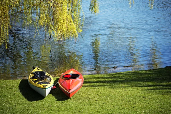 Dos kayaks yacen bajo un árbol en la hierba en la orilla de un lago, listo para la actividad de ocio —  Fotos de Stock