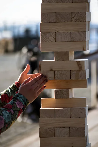 Jenga, as mãos da menina tentam arrancar um bloco de madeira, sem derrubar a torre, jogo de grupo de habilidade física com grandes blocos para ao ar livre — Fotografia de Stock