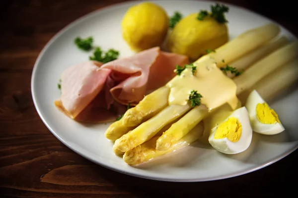 Bílý Chřest misky s brambory, šunkou, vejcem a omáčka na bílé plotně, rustikální načervenalé dřevěný stůl — Stock fotografie
