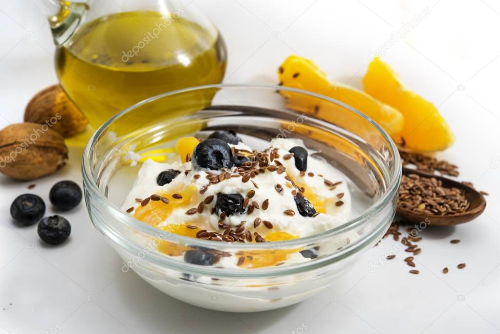 Healthy breakfast with quark or cottage cheese and linseeed oil, fresh blueberries, orange, walnut and flax seeds, light gray background