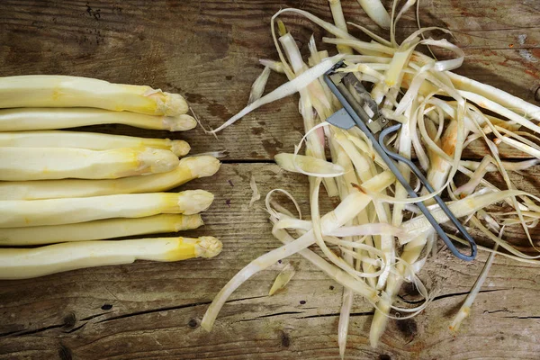 White asparagus and peel on a rustic wooden board, view from above — Stock Photo, Image