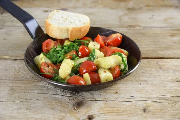 Fried vegetables in a black pan with asparagus, tomatoes and spinach on a rustic wooden table — Stock Photo, Image