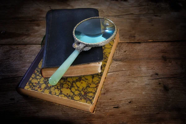 Vintage vergrootglas op twee antieke boeken, symbool voor wetenschap, onderzoek en kennis, op een oude rustieke houten tafel — Stockfoto