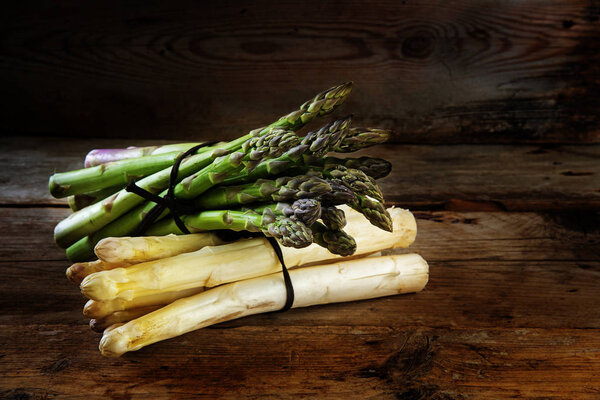 Зеленая и белая спаржа, свежая с рынка на темном деревенском деревянном столе
