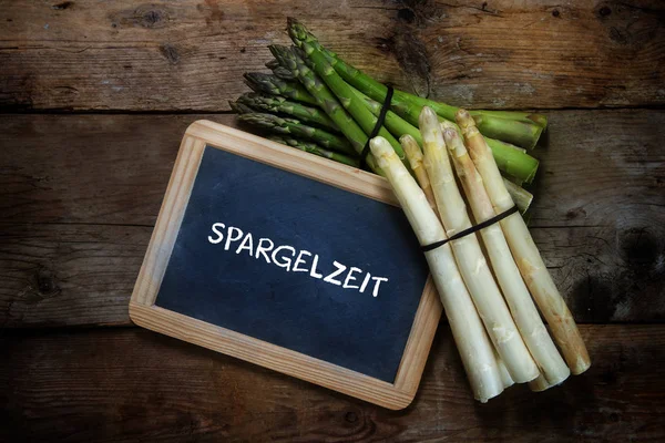 Green and white asparagus and a  blackboard with german text Spargelzeit, that means asparagus time, on a rustic wooden background