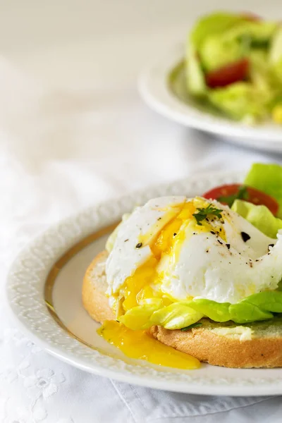 Ovo escalfado com gema de ovo em fatias de baguete com salada e tomate em um prato branco, delicioso café da manhã ou lanche, vertical, espaço de cópia — Fotografia de Stock