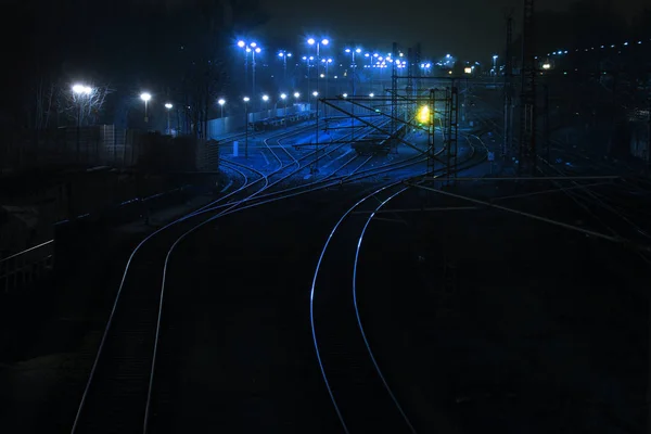 เส้นทางรถไฟในเวลากลางคืนนําแสงสว่างและโค้งไปที่สถานีขนส่งสินค้า, คัดลอกพื้นที่ในพื้นหลังที่มืด — ภาพถ่ายสต็อก