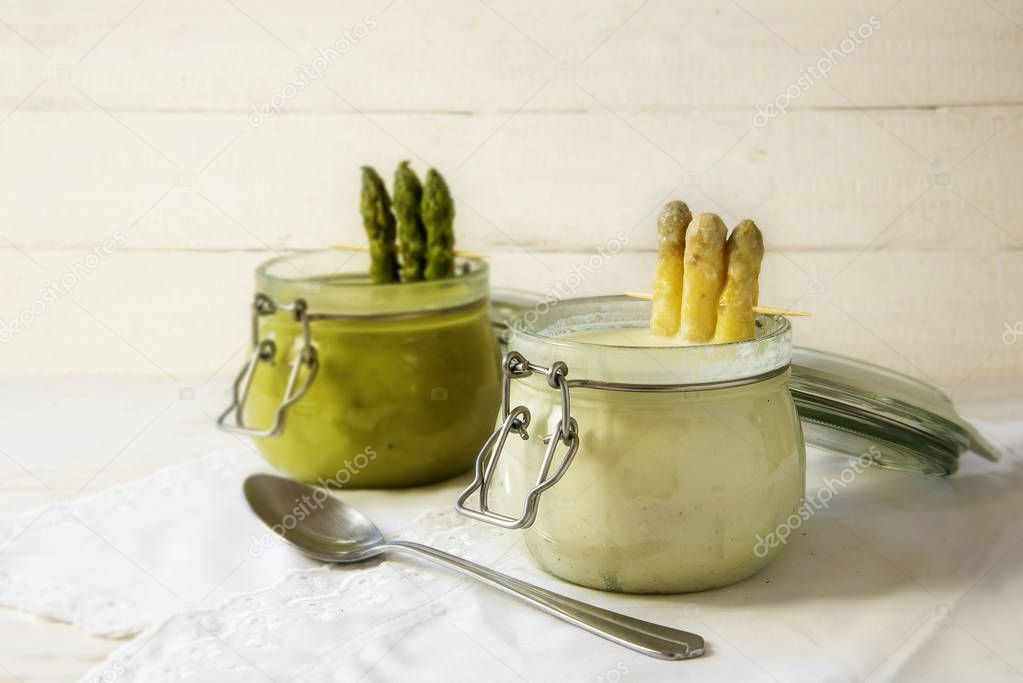 white and green asparagus cream soup in glass jars against a bright wooden background with copy space