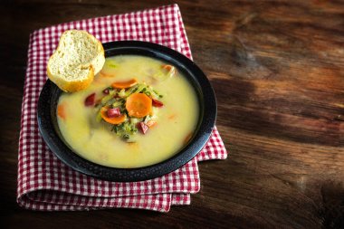  havuç, kırmızı biber, pırasa ve ekmek bir kırmızı beyaz peçete, rustik ahşap masa, büyük kopya alanı karanlık bir kase sebze çorbası