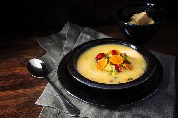 Sopa de crema vegetal con zanahorias, pimientos rojos y puerros en un bol moteado negro sobre madera rústica marrón, fondo oscuro con espacio para copiar —  Fotos de Stock