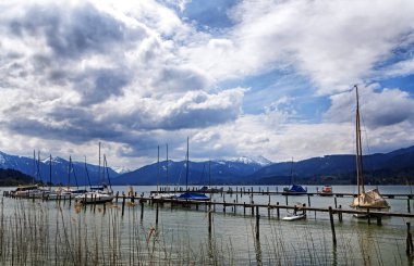Yelkenli tekne iskelesi tegernsee Gölü, karla kaplı dağlar ve mavi gökyüzü ile arka planda dramatik bulutlar üzerinde manzara ünlü turistik tatil beldesine Bavyera Alpleri