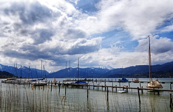 Barcos de vela en el embarcadero en el lago Tegernsee, montañas cubiertas de nieve y cielo azul con nubes dramáticas en el fondo, paisaje en el famoso complejo turístico en los Alpes bavarianos — Foto de Stock