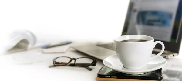 Xícara de café em uma mesa de escritório com telefone celular, laptop, óculos e papéis, fundo desfocado desaparece para branco, formato de banner panorâmico para cabeçalho da página web — Fotografia de Stock