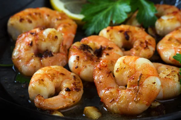 Prawns shrimps roasted in a black pan with garlic, lemon and italian parsley garnish, close up — Stock Photo, Image