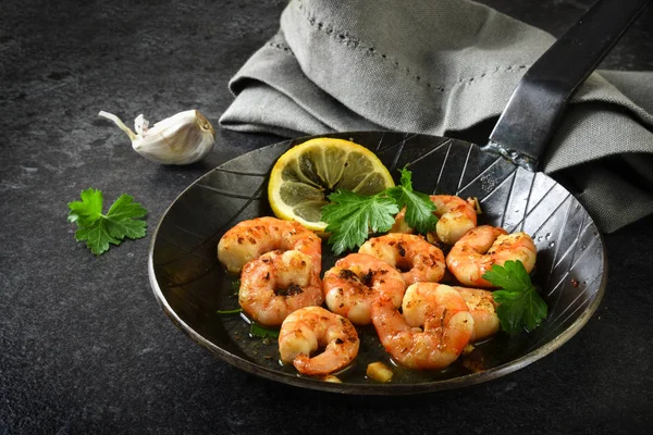 prawns shrimps with garlic, lemon, spices and italian parsley garnish in a black pan on a dark slate plate