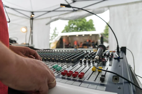 Mezclador de sonido en un festival de música al aire libre, vista sobre el panel de mezcla con deslizadores y micrófono, escenario borroso en el fondo — Foto de Stock