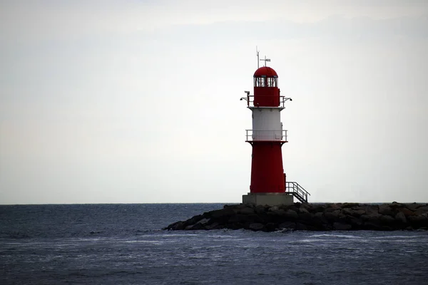 Faro rosso su pietre in mare in caso di maltempo contro un cielo grigio, Warnemuende al Mar Baltico, una destinazione turistica popolare in Germania, Europa — Foto Stock