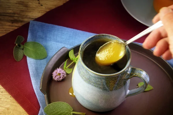 La miel fluye de una cuchara en una taza de té de hierbas con salvia y menta contra el resfriado o la gripe — Foto de Stock