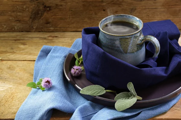 Cup of hot steaming herbal tea against cold wrapped in a blue cloth on rustic wood, copy space — Stock Photo, Image