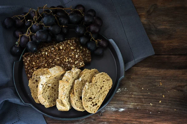 Dark and light wholemeal bread with seeds and blue grapes on a rustic wooden table — Stock Photo, Image