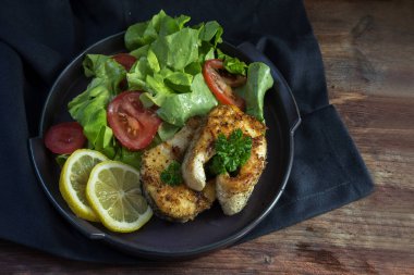 Kuzey pike kızarmış biftek ile limon, marul salatası, domates ve maydanoz garnitür siyah bir plaka üzerinde koyu ahşap masa, üstten üstten görünüm üzerinde sağlıklı düşük karbonhidrat yemek