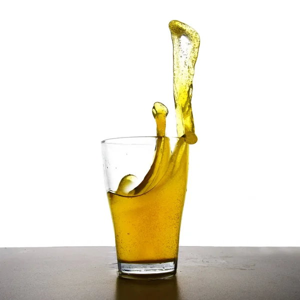 Bebida amarilla con salpicadura en un vaso, bebida refrescante de jugo de limón, refresco o té helado aislado sobre una mesa gris sobre un fondo blanco —  Fotos de Stock