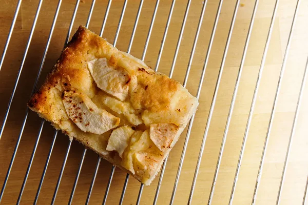 Piece of homemade apple cake on a baking grid over a light wooden table, overhead view from above, copy space — Stock Photo, Image