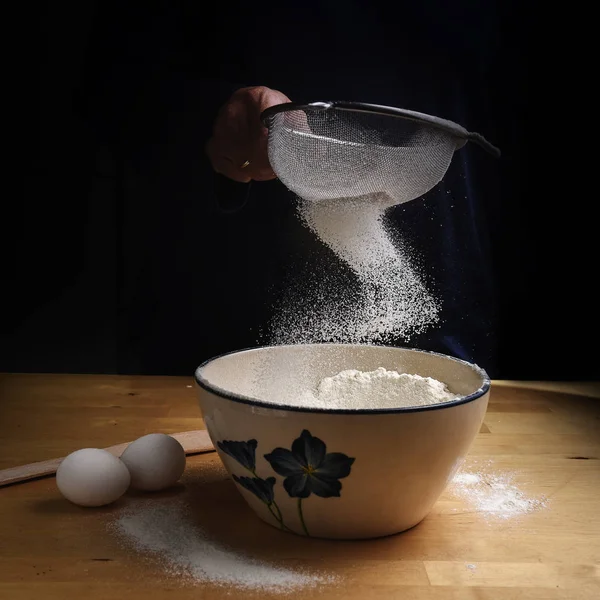 Bloem vallen in een boog van een zeef in een kom op een houten keuken aanrecht bij het bakken van voorbereiding, donkere achtergrond met kopie ruimte — Stockfoto