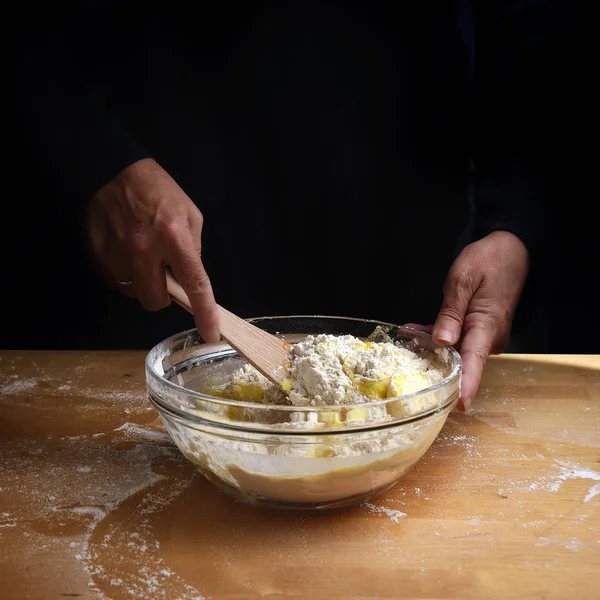 Weibliche Hände rühren Teig für Kuchen oder Brot in einer Schüssel auf einer hölzernen Küchenarbeitsplatte, Vorbereitung zum Backen, dunkler Hintergrund mit Kopierraum — Stockfoto