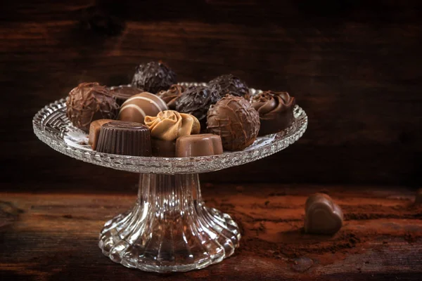 Cioccolato, assortimento di praline su un elegante piatto di vetro su uno sfondo di legno marrone, primo piano — Foto Stock