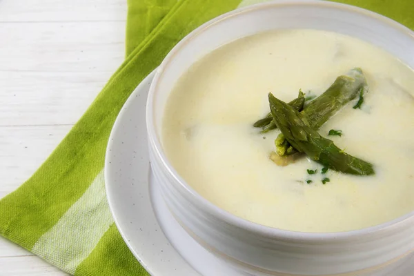 Soupe crème d'asperges blanches avec des têtes d'asperges vertes garnissent dans un bol, serviette verte, table blanche — Photo