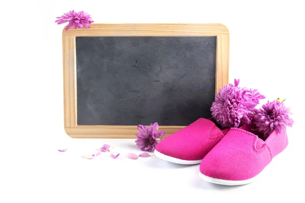 Zapatos de niño de color rosa y flores en frot de una pizarra de escritura con espacio de copia aislado sobre un fondo blanco, concepto Día Internacional de la Niña — Foto de Stock